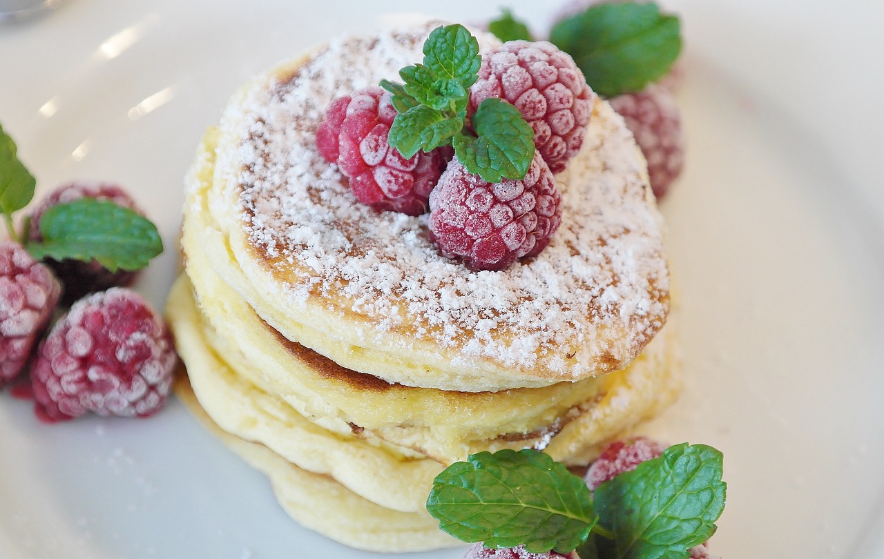 Pancake alla ricotta impilati su un piatto, decorati con frutta fresca e sciroppo.