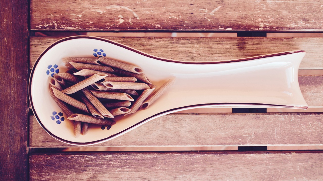 Due piatti di pasta, uno integrale e uno normale, con ingredienti freschi sul tavolo.