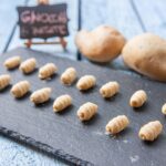 Gnocchi di patate freschi su un piano di lavoro con farina e attrezzi da cucina.