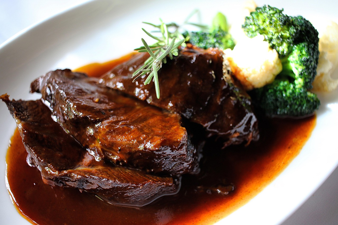 Brasato al vino rosso servito su un piatto, con contorni di verdure e un bicchiere di vino rosso accanto.