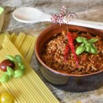 Pentola con ragù in cottura, ingredienti freschi e profumi avvolgenti in un ambiente di cucina rustica.