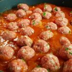 Polpette al sugo servite in un piatto, con pomodoro e prezzemolo fresco.