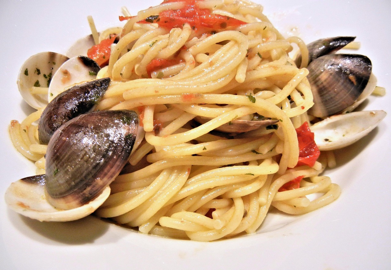 Spaghetti alle vongole serviti con prezzemolo fresco e pepe nero su un piatto bianco.