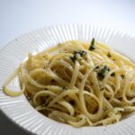 Pasta al limone con crema densa, guarnita con scorza di limone fresco e foglie di basilico.