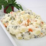 Insalata russa colorata con verdure e maionese, decorata per le feste su un piatto elegante.