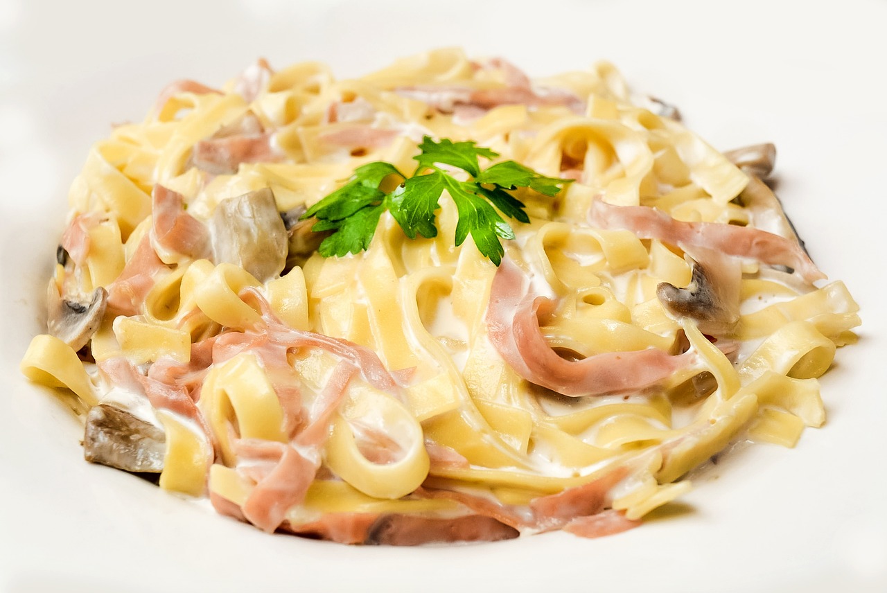 Pasta con panna e prosciutto in un piatto, decorata con prezzemolo fresco.