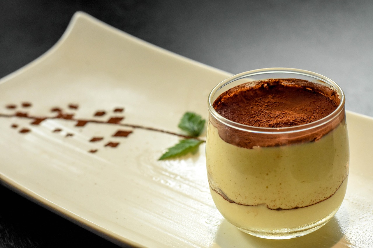 Tiramisù con crema liscia e compatta, decorato con cacao e caffè, in un piatto elegante.
