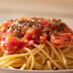 Spaghetti al pomodoro con salsa fumante, piatto decorato con basilico fresco.